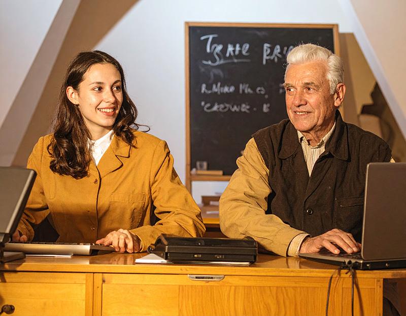 AI generated image of a college professor and a student sitting at a desk staring happily at their laptops; a blackboard behind them is visible with nonsense writing.